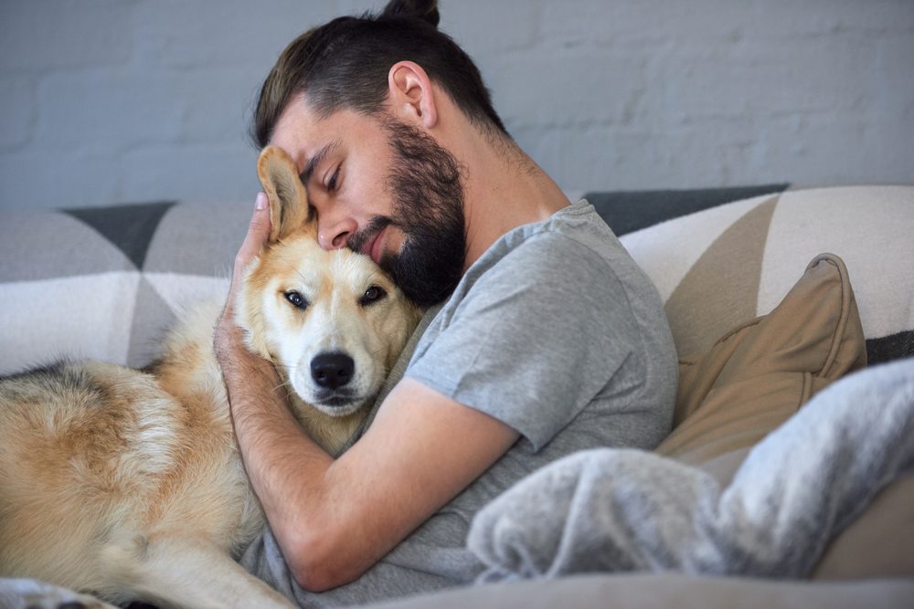 man hugging pet husky on couch